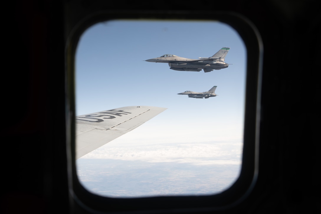 Two jets flying in formation by the wing of another aircraft.