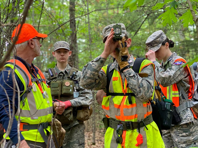 An airman wearing a neon vest holds a device to his eyes, while three other airmen also wear vests and take notes.