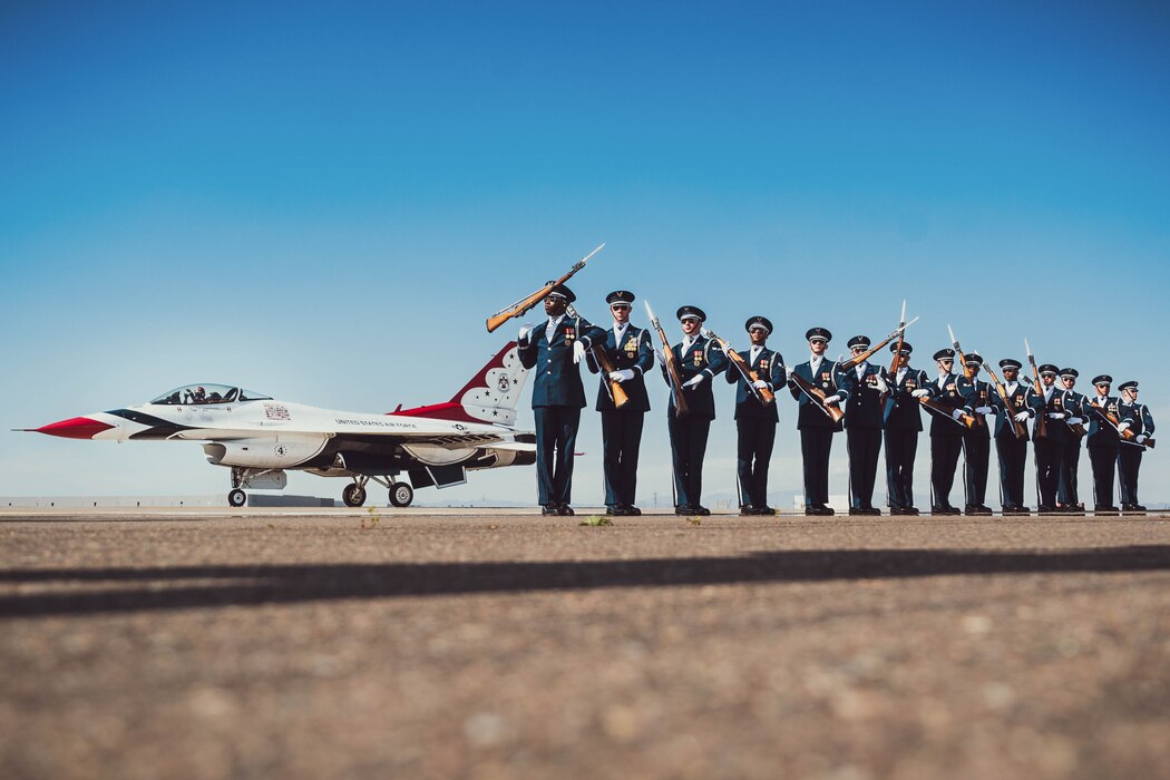 The U.S. Air Force Honor Guard conduct a drill while U.S. Air Force Maj. Jake Impellizzeri, U.S. Air Force Demonstration Squadron, “Thunderbirds” slot pilot No. 4., taxies down the runway to prepare for takeoff in an F-16 Fighting Falcons assigned to the Thunderbirds.