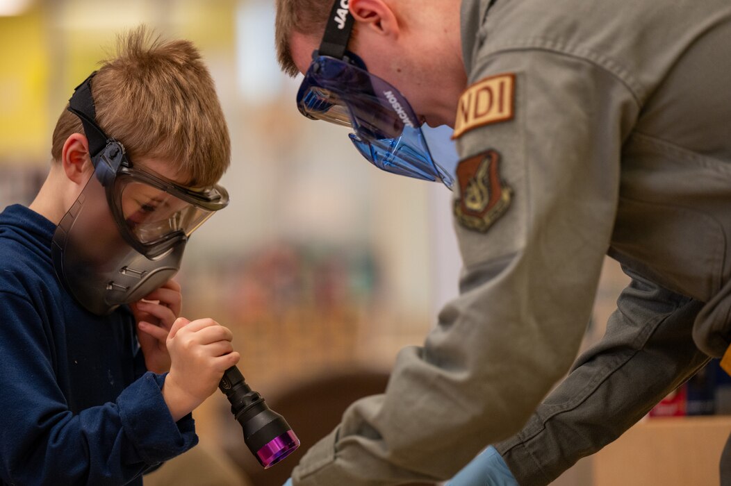 U.S. Air Force Senior Airman Gavin Woods, 51st Maintenance Squadron non-destructive inspection journeyman, shows an Osan Elementary School student how to check for fractures in metal objects during career day at Osan Air Base, Republic of Korea, March 15, 2024. Career day was hosted to provide OES students with a sense of excitement for going to school and give them information about future career options. (U.S. Air Force photo by Airman 1st Class Chase Verzaal)