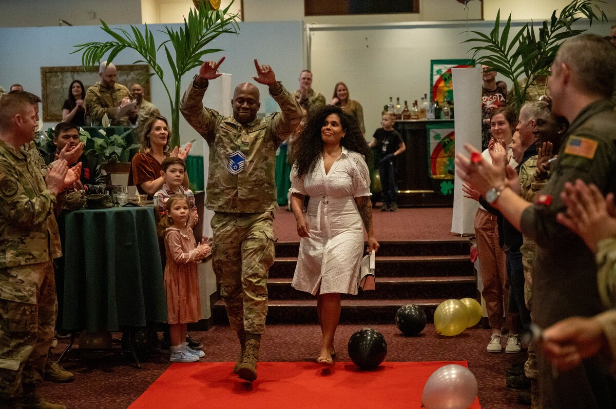 A service member raises his hands up in celebration as he walks to accept his award with his spouse.