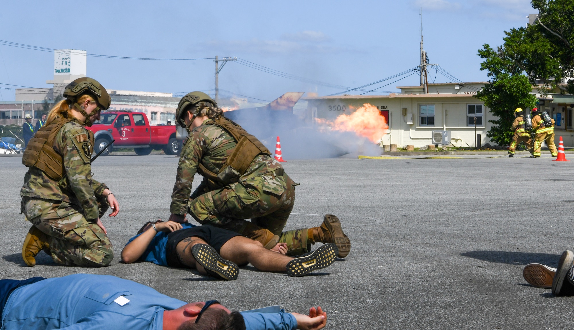 U.S. Air Force Senior Airman Autumn Encinias, left, 18th Security Forces Squadron response force leader, and U.S. Air Force Senior Airman Karleigh Morgan, 18th Security Forces Squadron pass and registration clerk, aid simulated victims while Okinawa emergency responders simulate extinguishing a controlled fire.