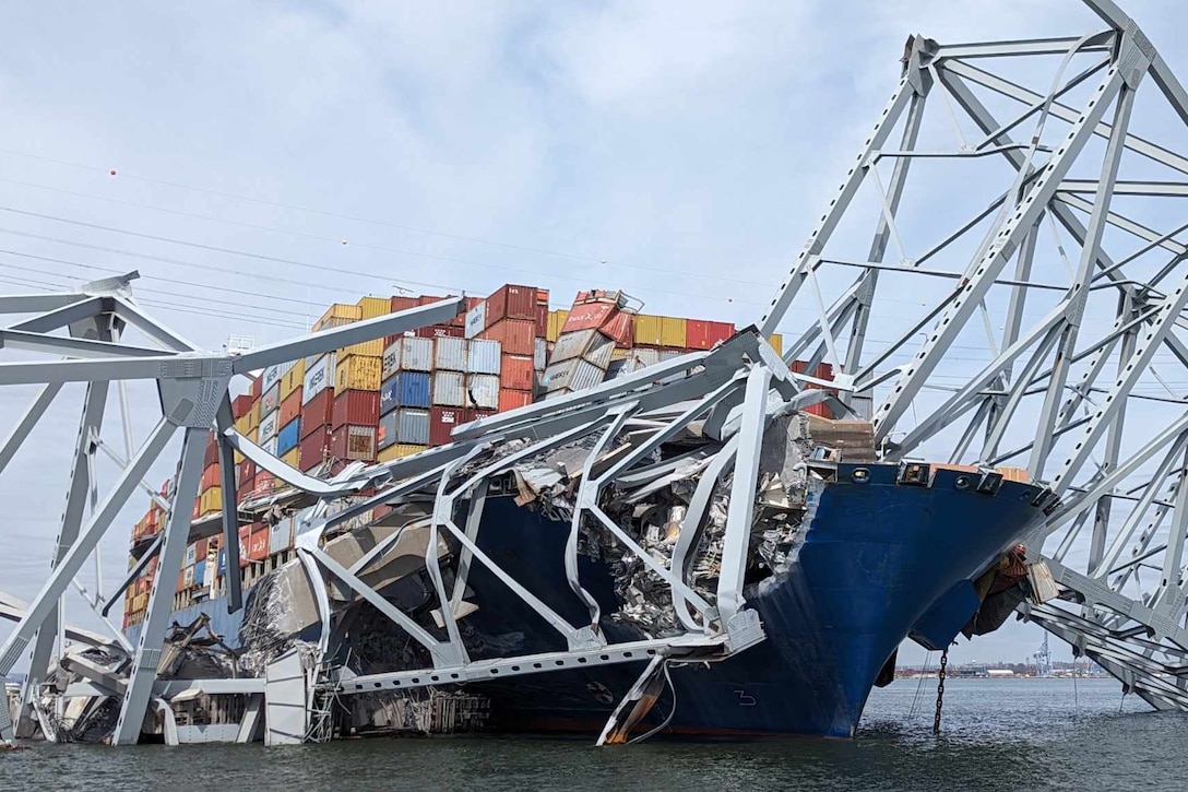 A metal bridge lies in pieces across a large container ship.