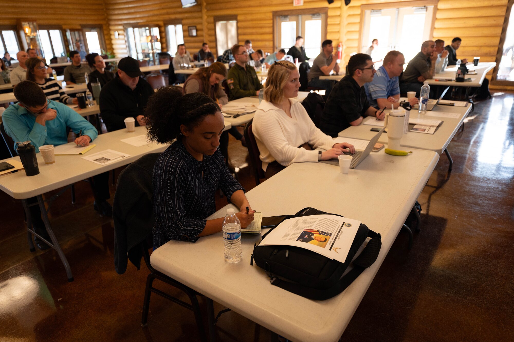 Rows of men and women at desks take notes, on paper as well as laptops.