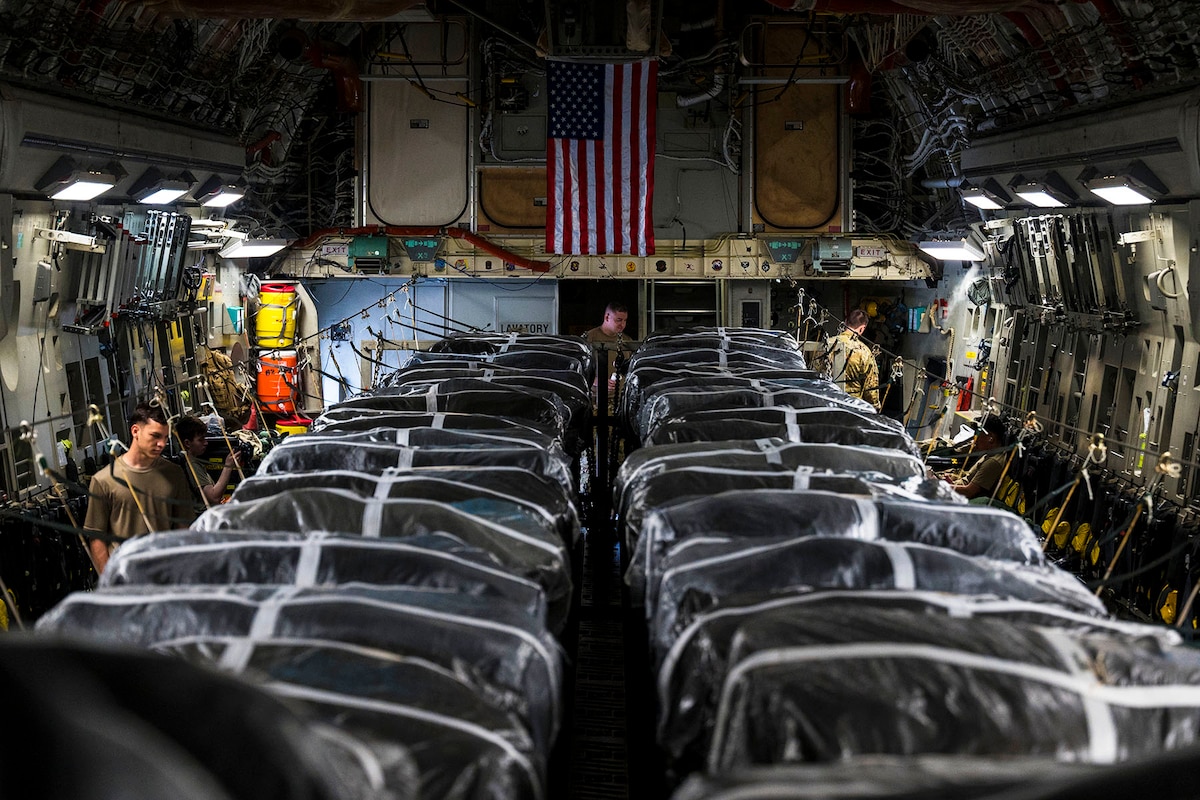 Airman work with large bundles of cargo inside an aircraft.
