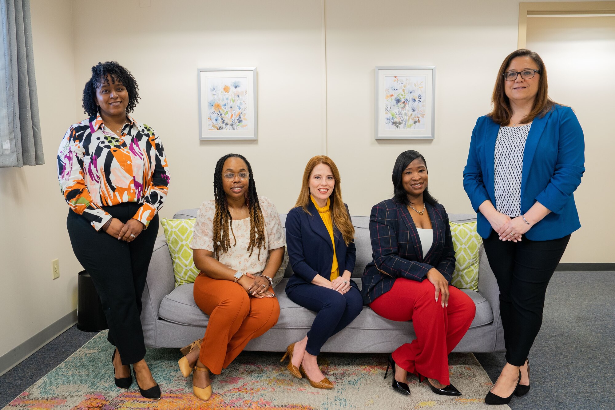 Three women sitting on a couch and two women standing are posed for a picture