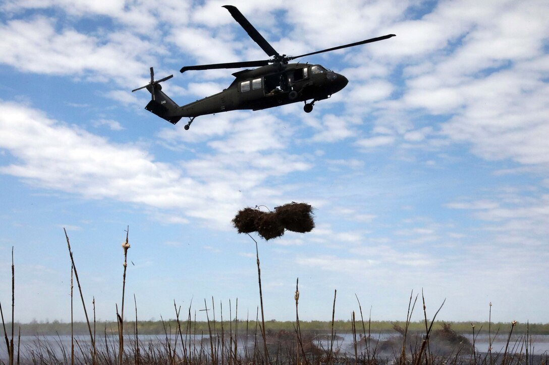 A helicopter drops a bundle of Christmas trees into a wetlands area.