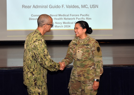 JOINT BASE SAN ANTONIO-FORT SAM HOUSTON – (March 25, 2024) – Rear Adm. Guido Valdes, commander, Naval Medical Forces Pacific (NMFP), presents his command coin to U.S. Army Sgt. Gabriela Jordan of Naval Medical Research Unit (NAMRU) San Antonio during a townhall meeting held at the Military and Family Readiness Center. Valdes, who serves as the Chief of Navy Medical Corps, has oversight of 10 Navy Medicine Readiness and Training Commands on the West Coast and Pacific Rim as well as Navy Medicine's eight global research labs. Valdes also serves under the Defense Health Agency (DHA) as the director of the Defense Health Network Pacific Rim where he oversees the delivery and integration of healthcare at nine medical treatment facilities (MTF) on the West Coast and Pacific Rim. NAMRU San Antonio’s mission is to conduct gap driven combat casualty care, craniofacial, and directed energy research to improve survival, operational readiness, and safety of Department of Defense (DoD) personnel engaged in routine and expeditionary operations. It is one of the leading research and development laboratories for the U.S. Navy under the DoD and is one of eight subordinate research commands in the global network of laboratories operating under the Naval Medical Research Command in Silver Spring, Md. (U.S. Navy photo by Burrell Parmer, NAMRU San Antonio Public Affairs/Released)