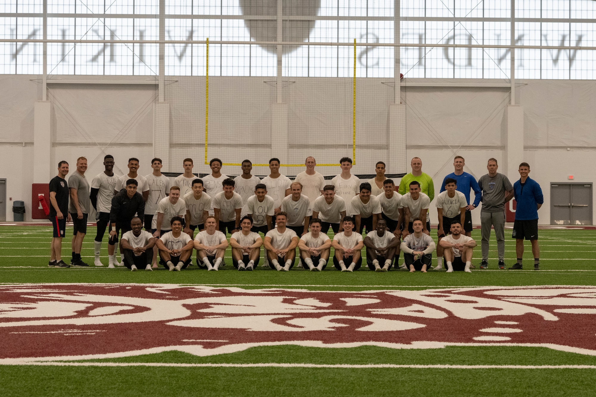 A photo of people lined up for a group photo, sitting on a soccer field.