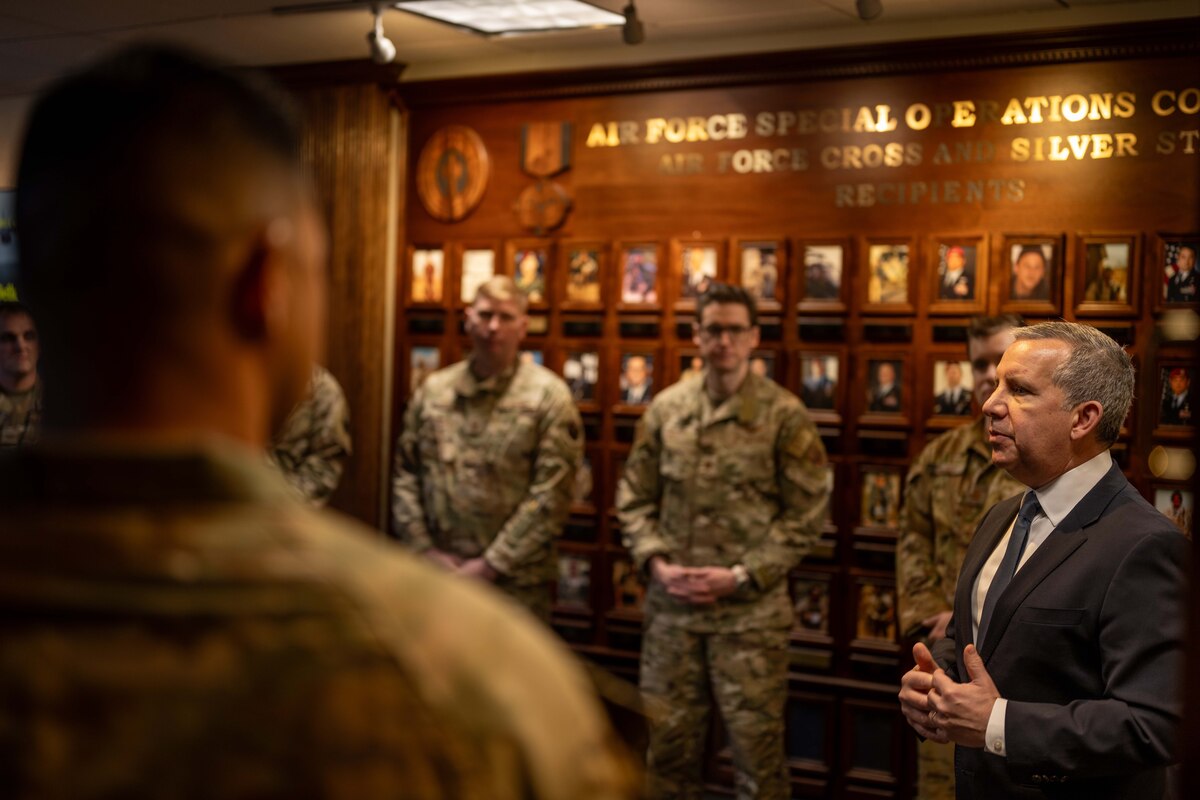 A man in civilian attire speaks with members of the military.