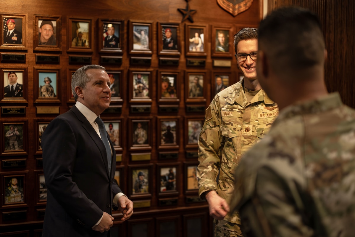 A man in civilian attire speaks with members of the military.