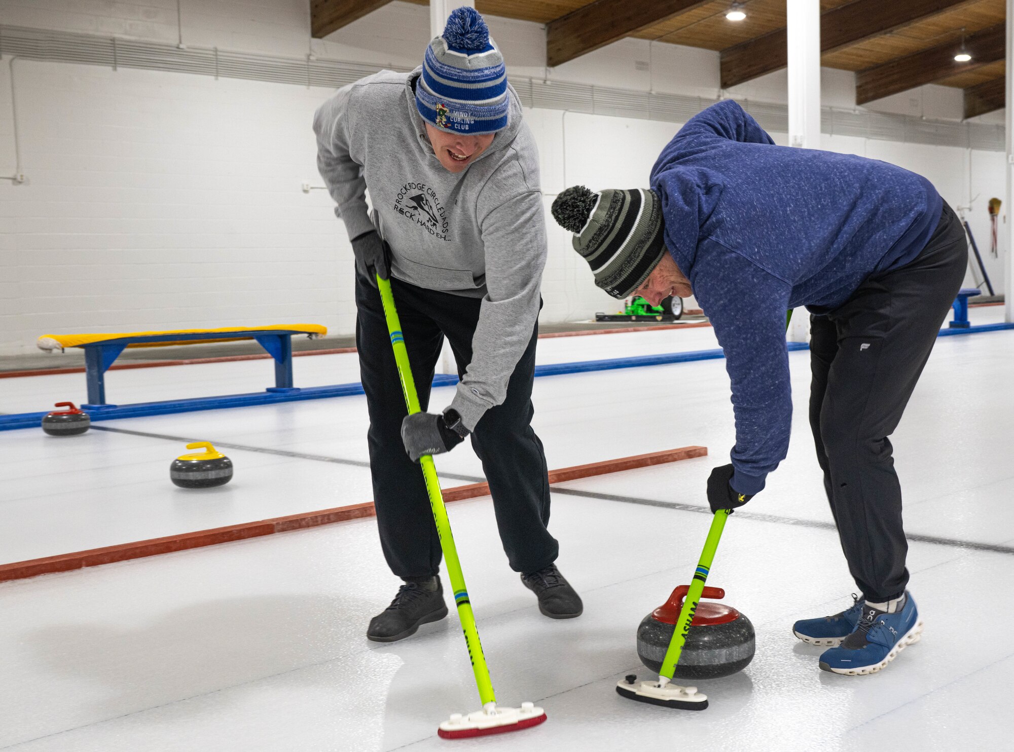 U.S. Air Force Lt. Col. Darrell Gibson, 740th Missile Squadron commander (left), and U.S. Air Force Maj. Zachary Jones 91st Operations Group wing operations center director, sweep the ice in the path of a curling stone at the Minot Curling Club, Minot, North Dakota, March 19, 2024. Gibson and Jones swept a path for the curling stone to better direct it towards the target area. (U.S. Air Force photo by Airman 1st Class Kyle Wilson)
