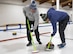U.S. Air Force Lt. Col. Darrell Gibson, 740th Missile Squadron commander (left), and U.S. Air Force Maj. Zachary Jones 91st Operations Group wing operations center director, sweep the ice in the path of a curling stone at the Minot Curling Club, Minot, North Dakota, March 19, 2024. Gibson and Jones swept a path for the curling stone to better direct it towards the target area. (U.S. Air Force photo by Airman 1st Class Kyle Wilson)