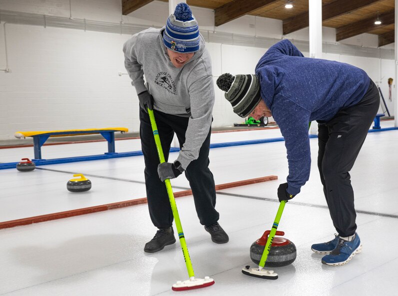 U.S. Air Force Lt. Col. Darrell Gibson, 740th Missile Squadron commander (left), and U.S. Air Force Maj. Zachary Jones 91st Operations Group wing operations center director, sweep the ice in the path of a curling stone at the Minot Curling Club, Minot, North Dakota, March 19, 2024. Gibson and Jones swept a path for the curling stone to better direct it towards the target area. (U.S. Air Force photo by Airman 1st Class Kyle Wilson)