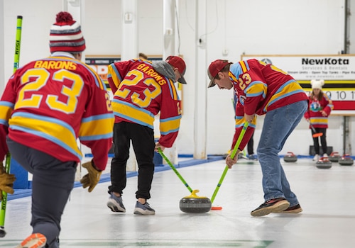 Members of the Lobstahs curling team execute the delivery of a curling stone at the Minot Curling Club, Minot, North Dakota, March 19, 2024. The delivery, or throw, is the process of sliding the curling stone down the sheet of ice and directing it towards the target area. (U.S. Air Force photo by Airman 1st Class Kyle Wilson)