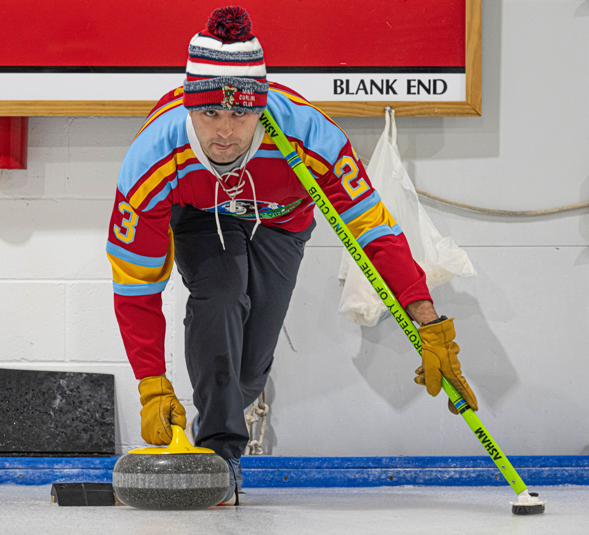 U.S. Air Force Capt. Steven Lawless, 23rd Bomb Squadron weapon systems officer, prepares to execute the delivery of a curling stone at the Minot Curling Club, Minot, North Dakota, March 19, 2024. Lawless used his broom for stability during the process of delivering the stone. (U.S. Air Force photo by Airman 1st Class Kyle Wilson)