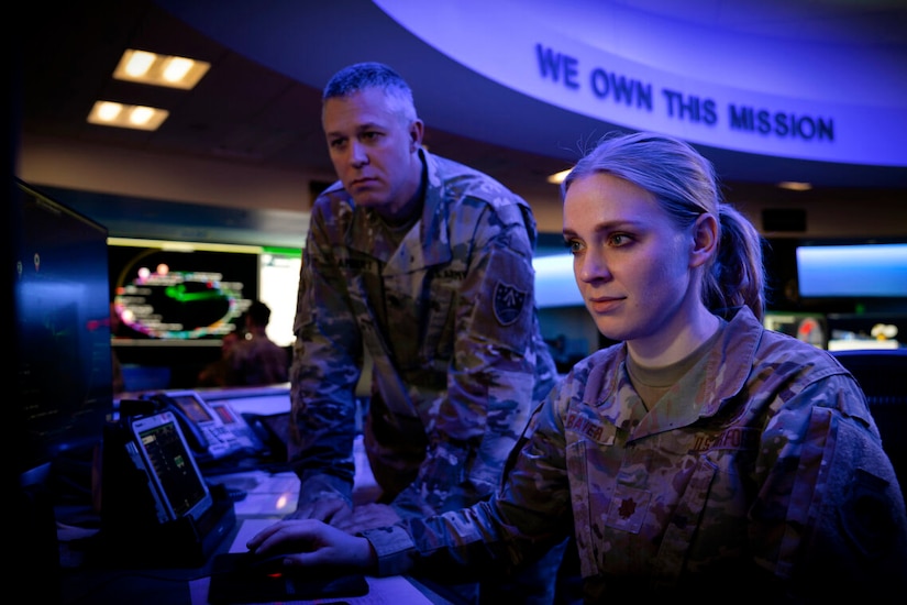 Service members in uniform look at a computer terminal.