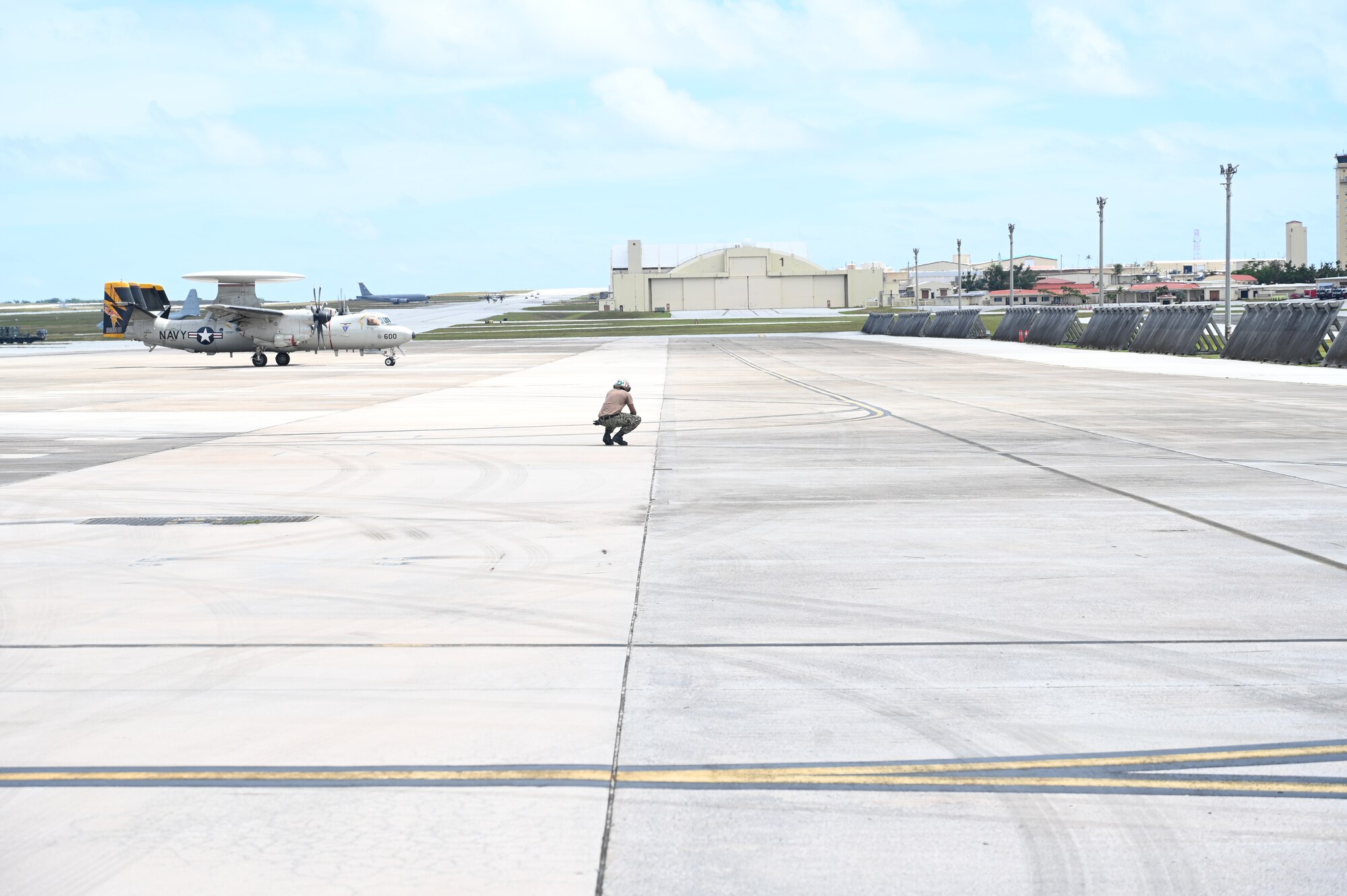 A Sailor waits for an E-2D Hawkeye aircraft to finish its taxi on the flightline.