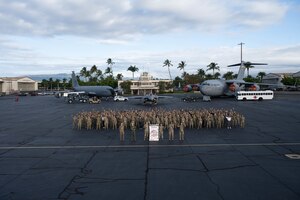 Women assigned to Joint Base Pearl Harbor Hickam stand for a group photo with static aircraft in the background