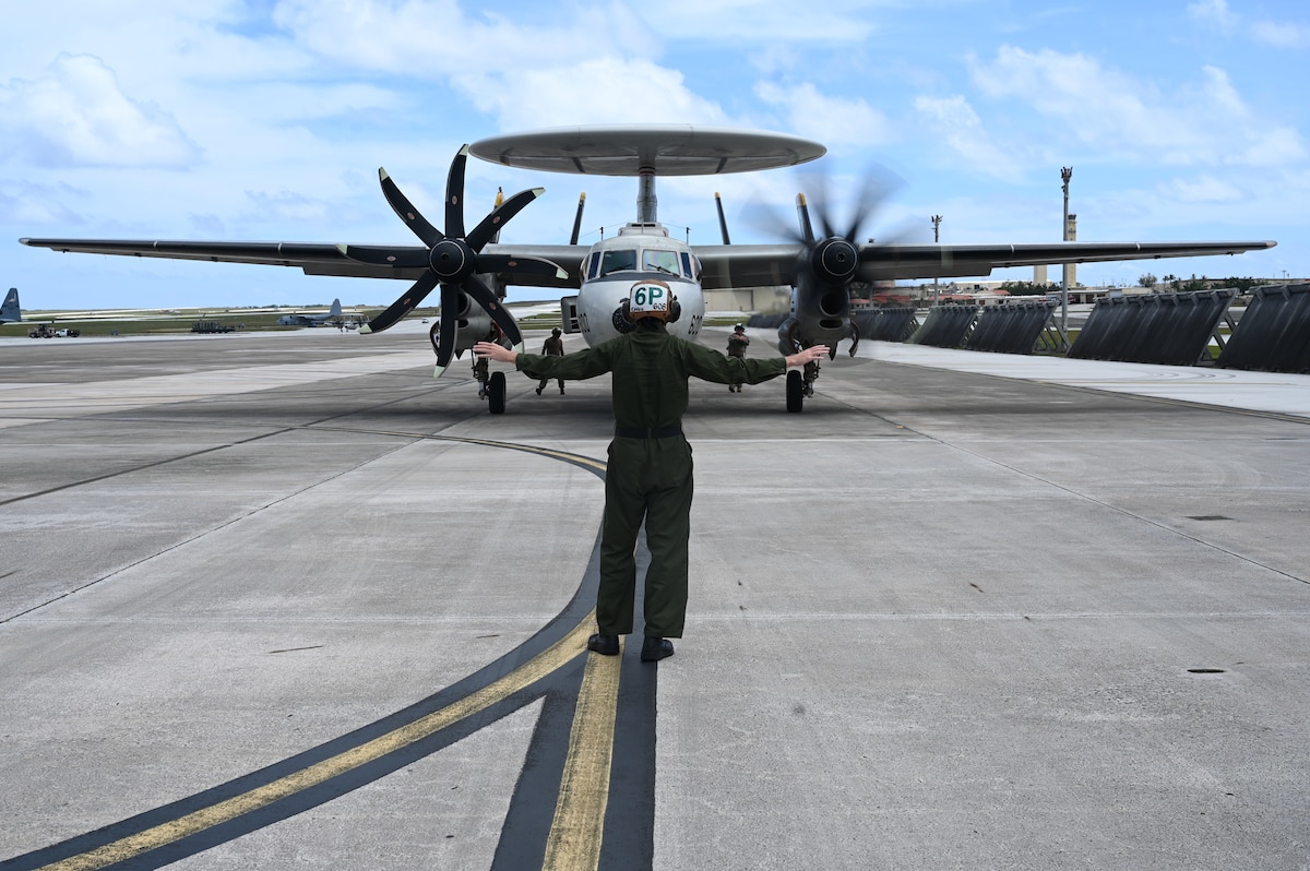 A Sailor guides a E-2D Hawkeye aircraft on the flightline.