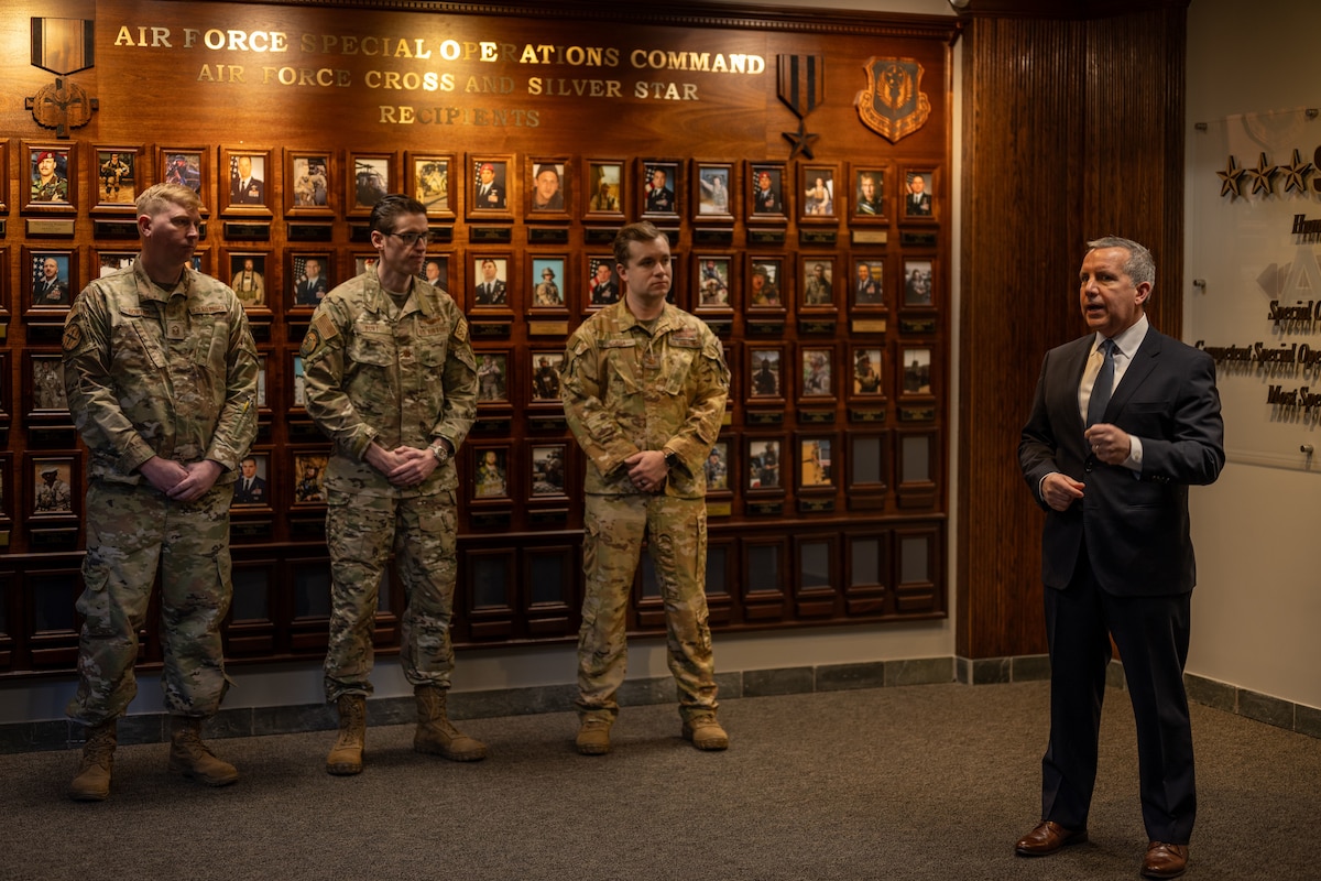 A man in civilian attire speaks with members of the military.