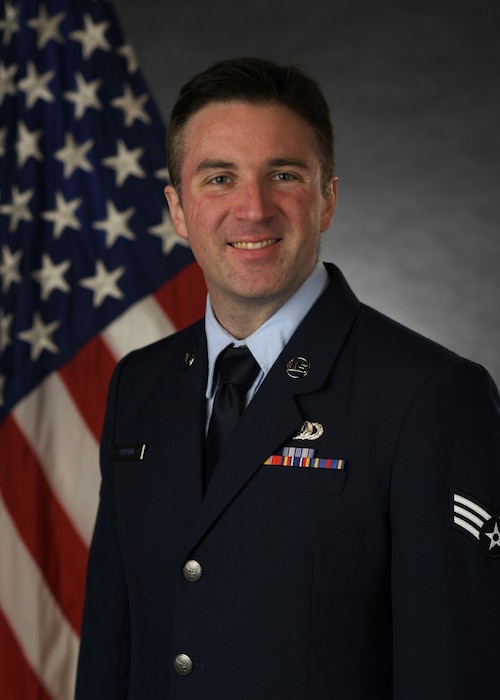 Official Photo of SrA Henry Gergen, regional band- jazz trumpet.  SrA Gergen  is wearing blue service dress in front of the American flag.