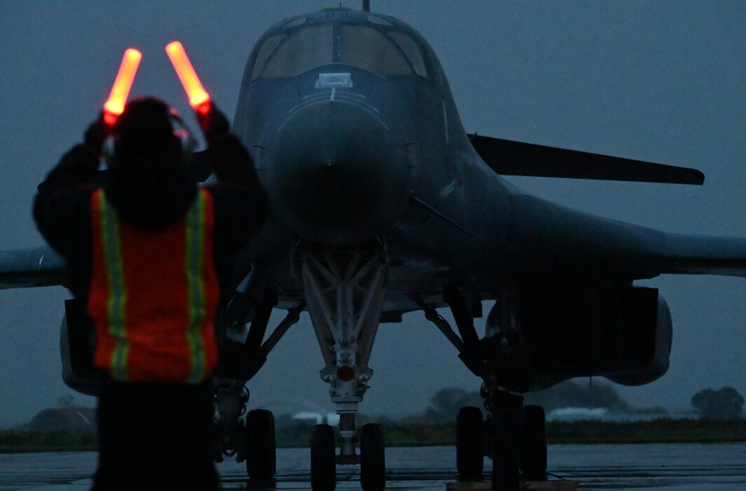 A maintainer in the foreground waves in a large bomber on a dark rainy day