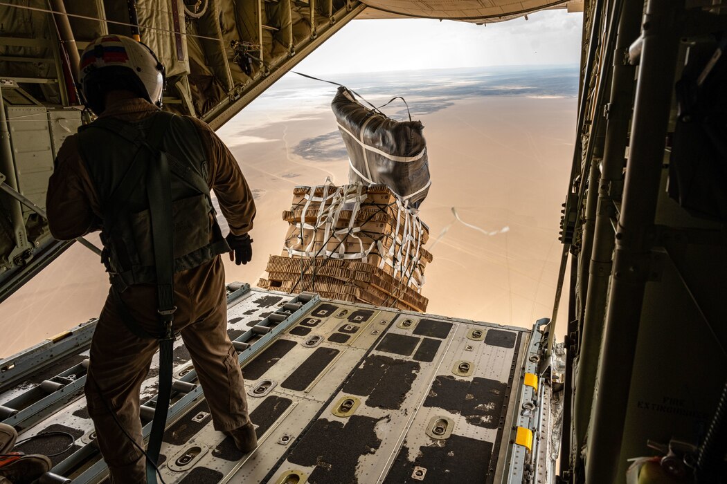 A Marine watches as a cargo pallet falls from the back of an open aircraft cargo ramp for a supply drop.