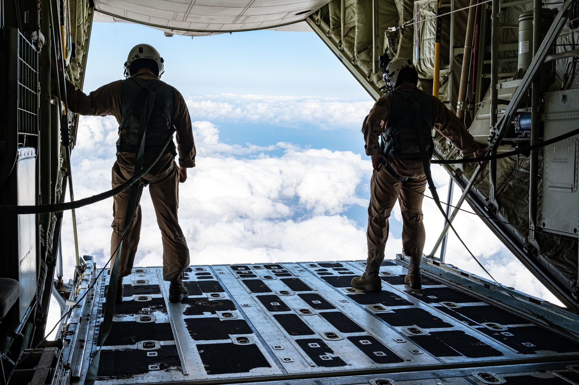 Two Marines in flight suits stand on an open aircraft cargo ramp, looking out.