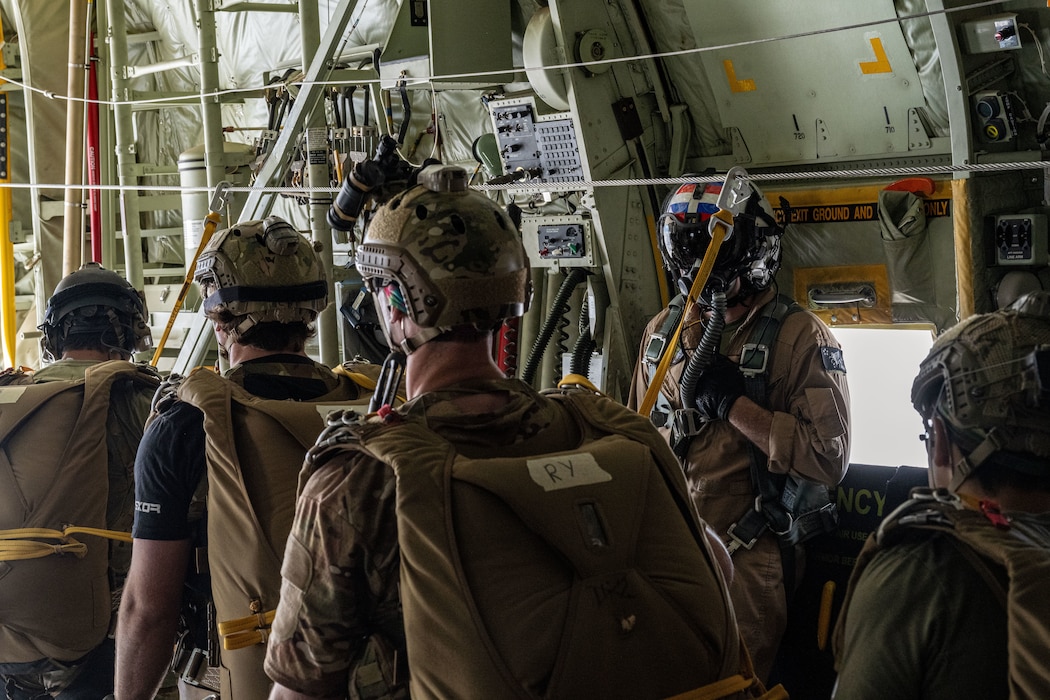 Air Force pararescuemen stand in a row on an aircraft, holding static lines for parachute jumps.