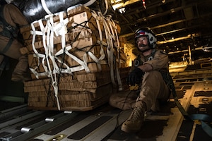 A Marine sits next to a cargo pallet on an aircraft.