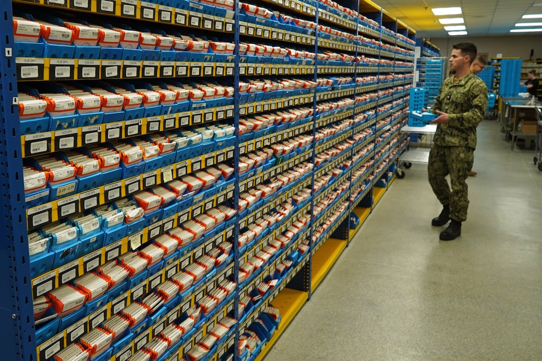 A service member stands in front of large shelves of packages.