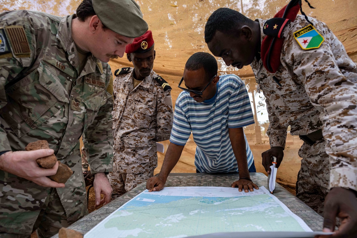Service members and a civilian stand around a small table and look at a map.