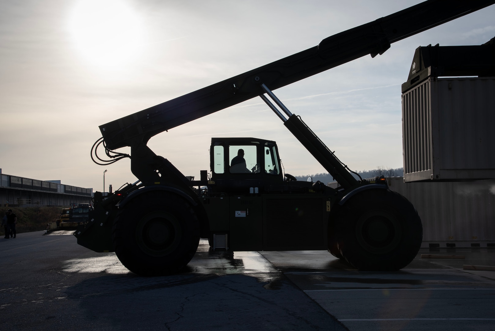 Man in the cab of heavy machinery, silhouetted against a cloudy morning sky.