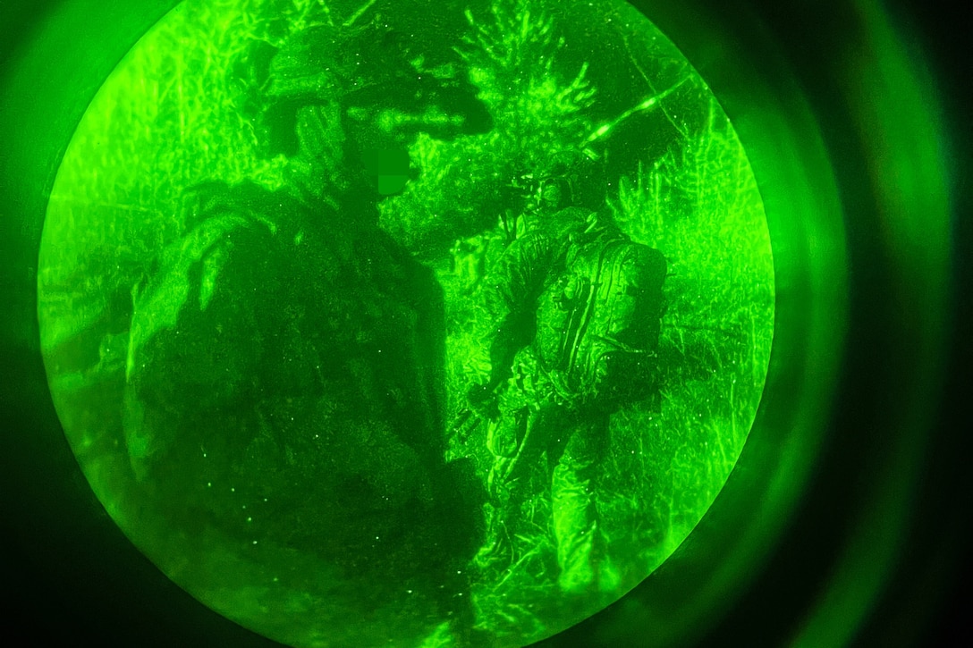 Uniformed service members provide security at night. They are illuminated by a green light and photographed through a scope.