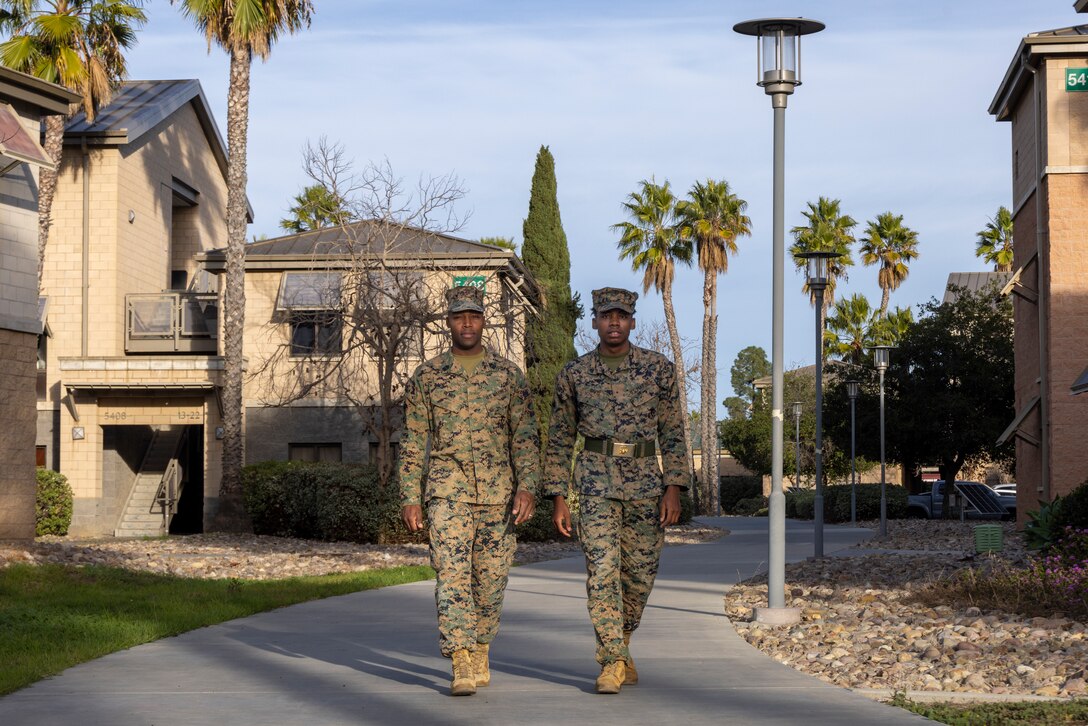 Two Marines in uniform walking on a sidewalk in a suburb.