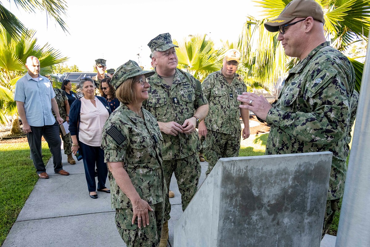 People in military camouflage stand outside talking as others in civilian clothing look on in the background.