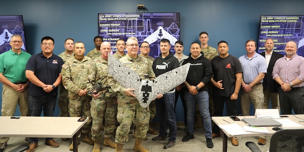Photo of 15 national guard soldiers and two instructors in a classroom. One of the guradsmen is holding an unmanned aerial drone.