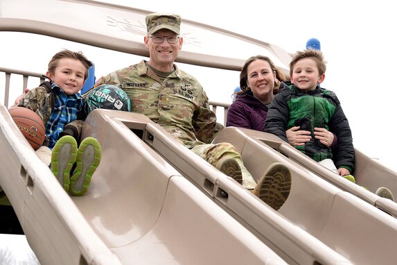 Maj. Trevor Wiegers, Mission Command Training Program observer coach/trainer and his wife Erin Wiegers, Fort Leavenworth Army Military Pay Office military pay technician, play after school with their children, Tristan (far left) and Trajan, at the Eisenhower Elementary School playground at Fort Leavenworth, Kansas March 22, 2024. A recent U.S. Army Financial Management Command initiative ensures AMPO employees who relocate with their service member spouses during permanent changes of station will maintain their positions within the command. (U.S. Army photo by Prudence Siebert)