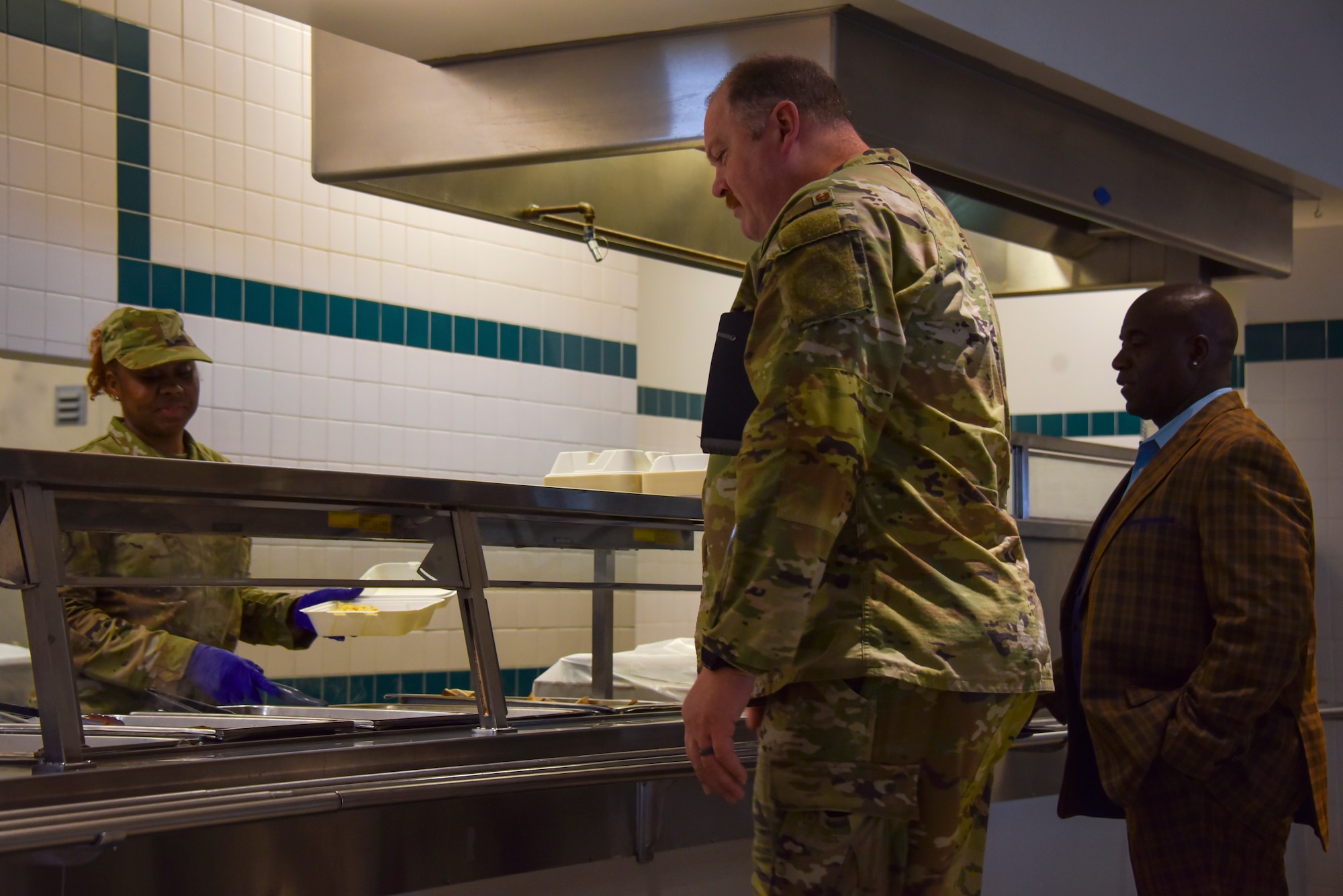 A military member serves food to people.