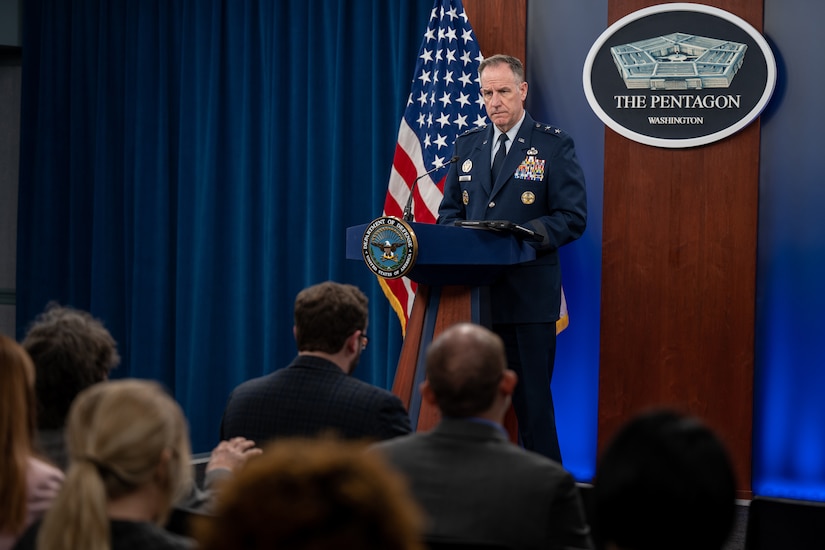 An Air Force general stands behind a lectern facing a seated audience.