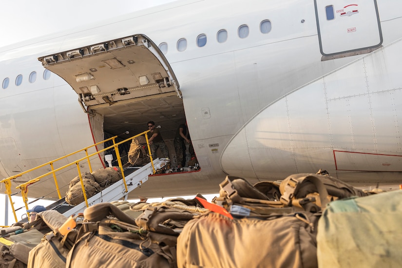 A person in a military uniform unloads bags from inside an airplane.