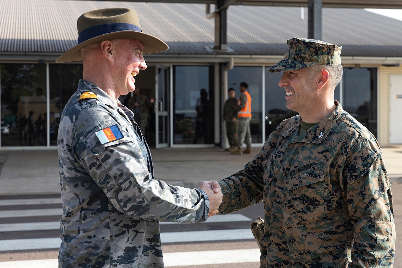 Two service members in military uniforms shake hands.