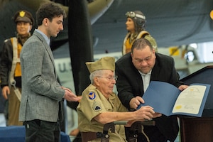 U.S. Army Air Corps veteran Staff Sgt. William Bieber, center, is presented a proclamation from the Delaware Commission of Veteran Affairs by John Taylor, Air Mobility Command Museum director, right, during a ceremony held at the museum on Dover Air Force Base, Delaware, March 26, 2024. During WWII, Bieber served as a B-24 Liberator ball turret gunner in the Western Pacific. He flew 10 missions and downed one Japanese Zero aircraft. (U.S. Air Force photo by Roland Balik)