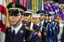 Several people dressed in various military uniforms are standing in a row while holding a mix of flags and rifles.