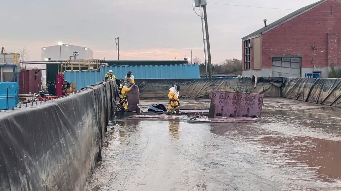 People in hazardous materials protective clothing work in a large pool of water inside an environmental remediation site.