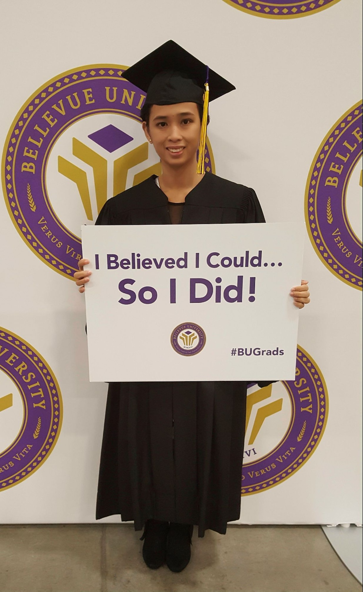 Graduate in robes holds a sign that reads "I believed I could so I did!"