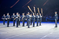 military personnel spin rifles during a performance before a large indoor audience