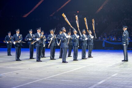 military personnel spin rifles during a performance before a large indoor audience