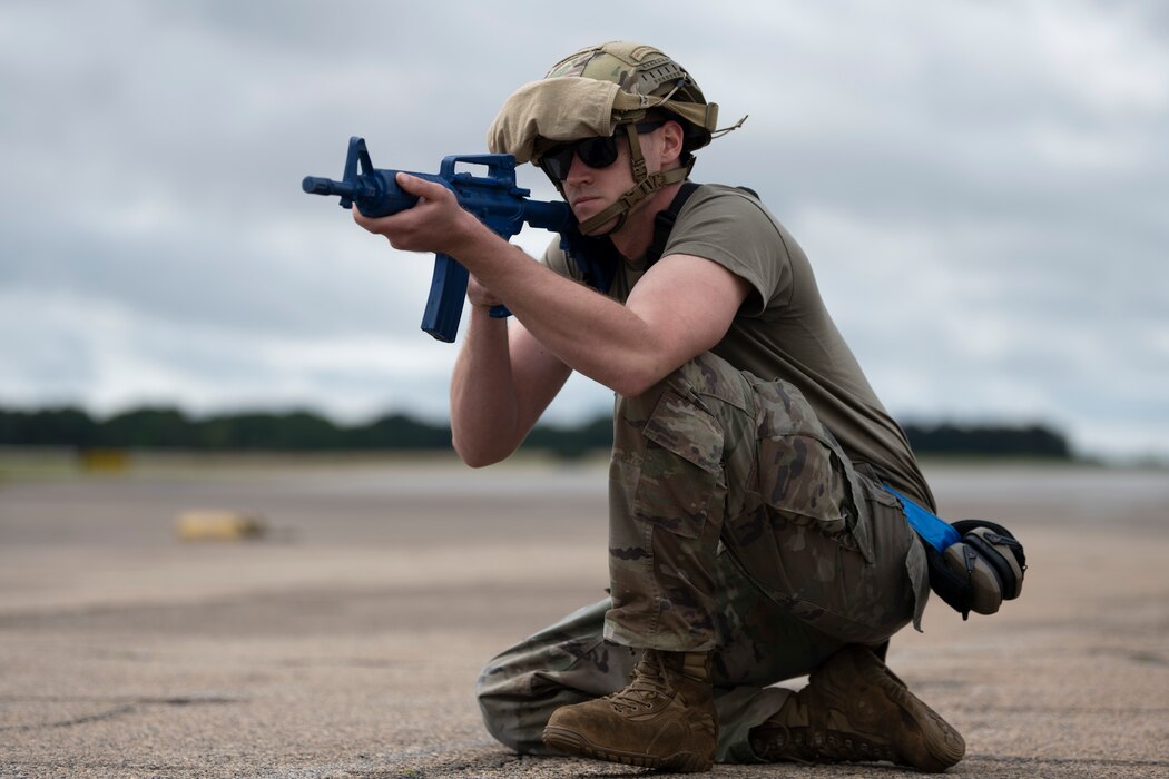 A person squatting in a defensive stance, holding a dummy gun.